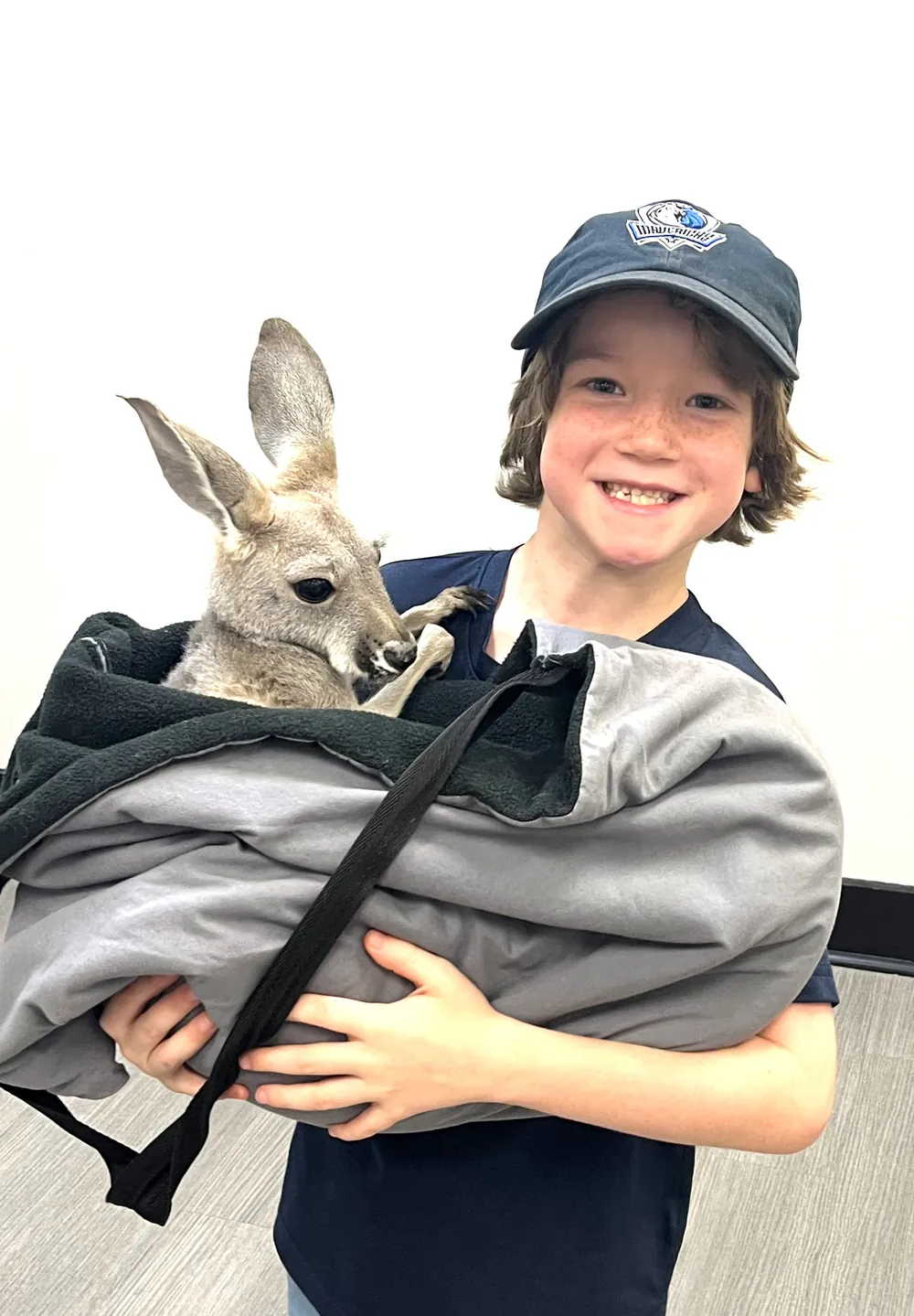 A smiling student holds a young kangaroo wrapped in a carrying pouch.